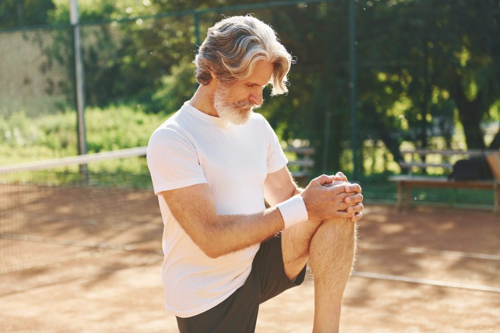 senior man in tennis court holding his knee