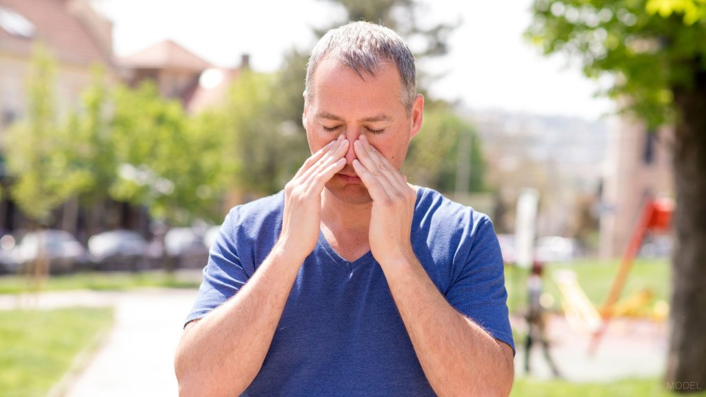 Middle aged man (MODEL) holding his painful nose area with both hands.