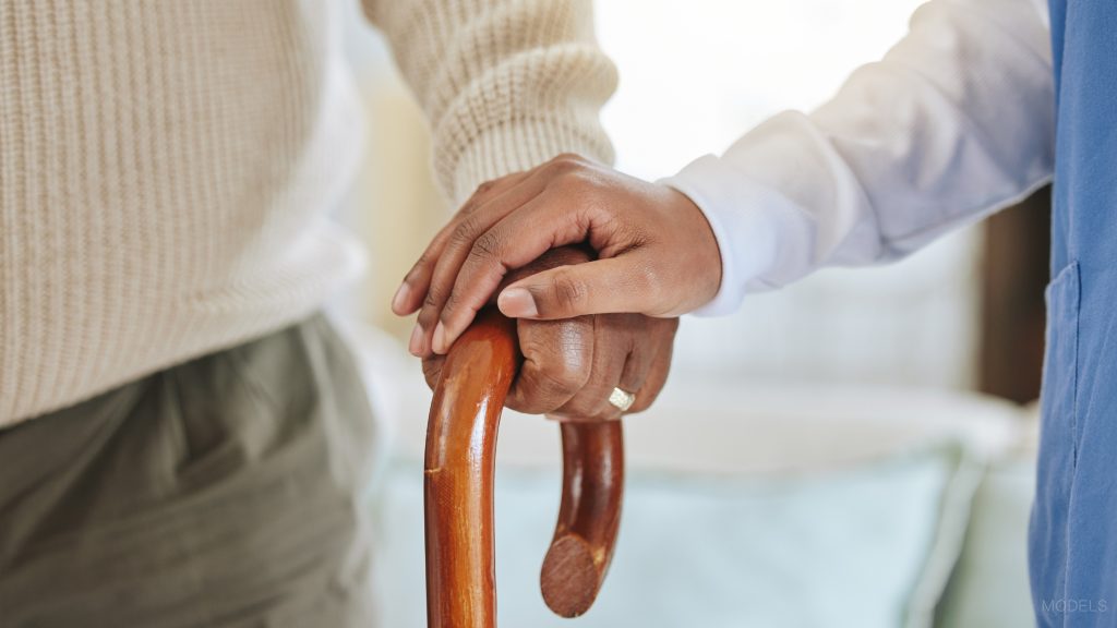 Doctor in white coat is holding a patient's (hand (MODELS) while walking with a wooden cane.