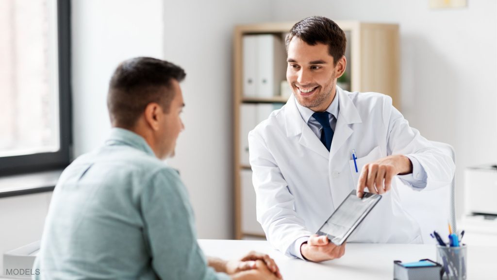 A doctor is talking to a patient at a desk. (Models)