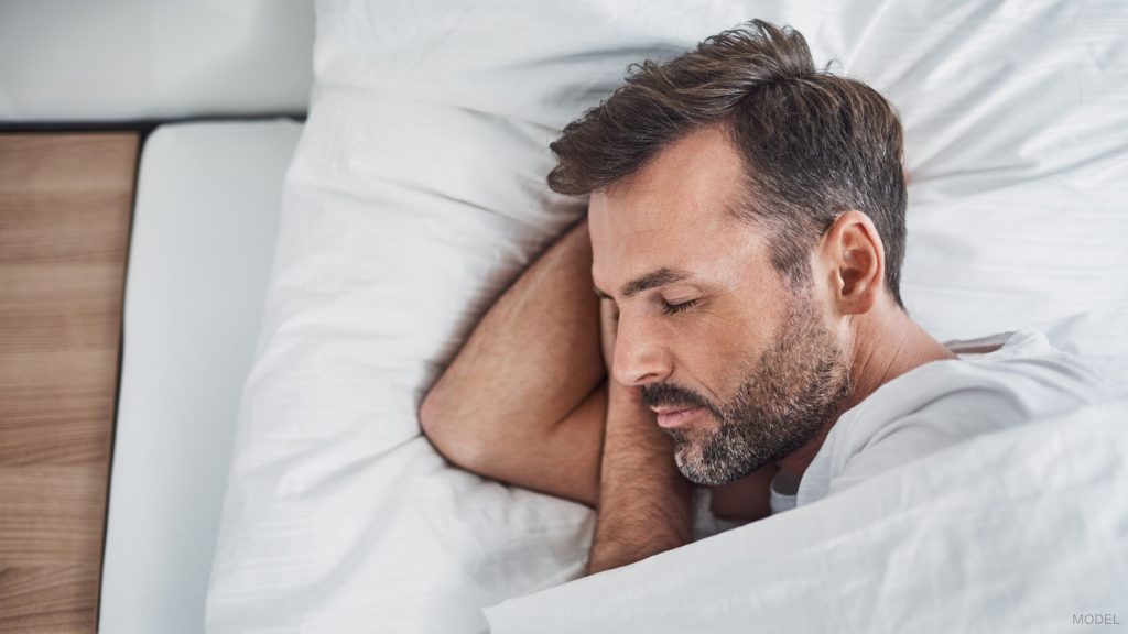 A man sleeping in bed facing their side. (Model)
